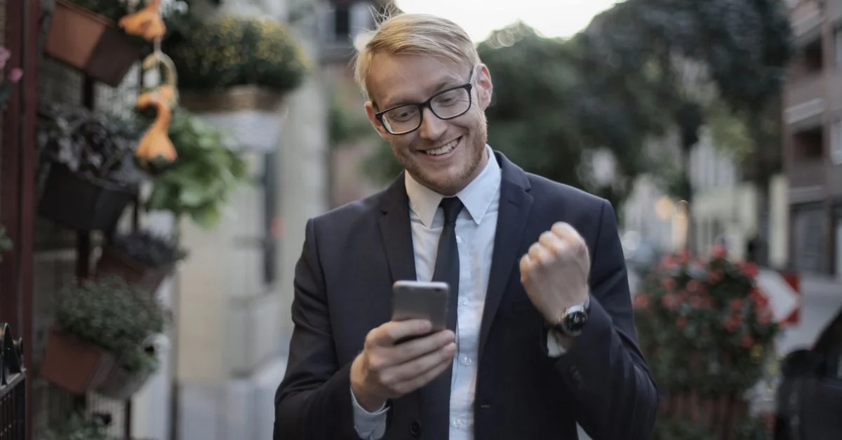 Jeune professionnel excité célèbre son succès en plein air avec un téléphone mobile dans un cadre urbain.