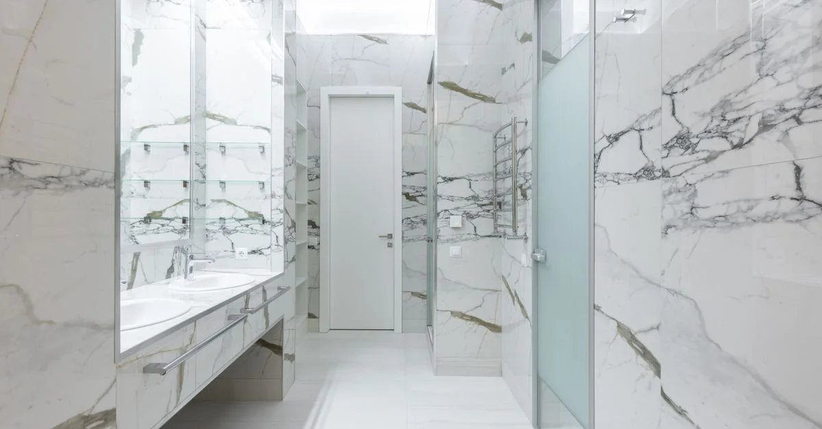 Salle de bain contemporaine avec des carreaux en marbre, des doubles lavabos et des équipements modernes affichant un style lumineux et luxueux.