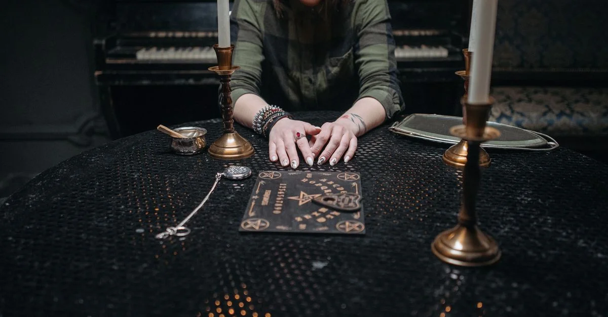 Femme assise à une table avec des bougies et un plateau de Ouija, ambiance feutrée.