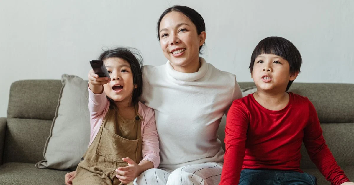 Mère et enfants passant du temps ensemble à l'intérieur, regardant la télévision et souriant.