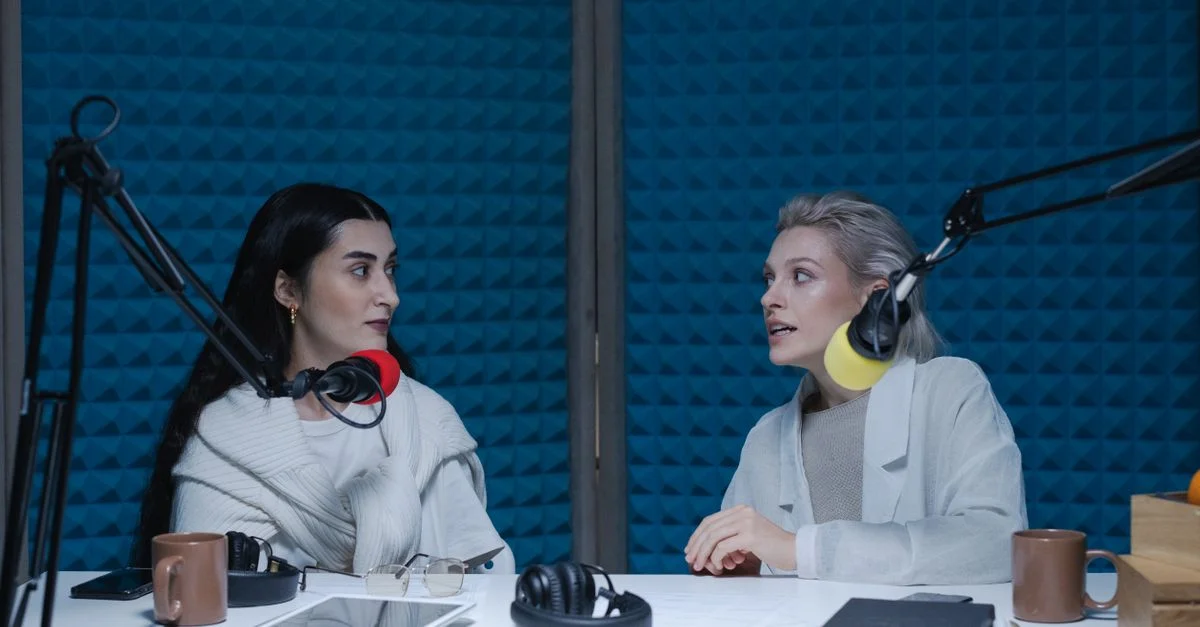 Deux femmes engagées dans une conversation, enregistrant un podcast dans le studio avec des microphones et des écouteurs.
