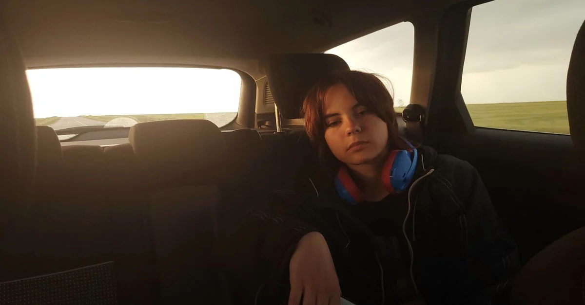 Fille adolescente assise dans une voiture, se relaxant avec des écouteurs pendant une conduite au coucher du soleil.
